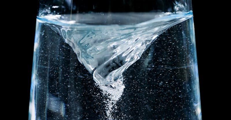 Close-up of a mesmerizing water vortex in a glass with droplets against a dark background.